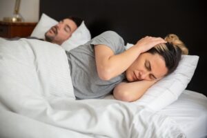 https://www.pexels.com/photo/a-frustrated-woman-trying-to-sleep-7556638/ Man snoring next to woman in bed with the woman covering her ears